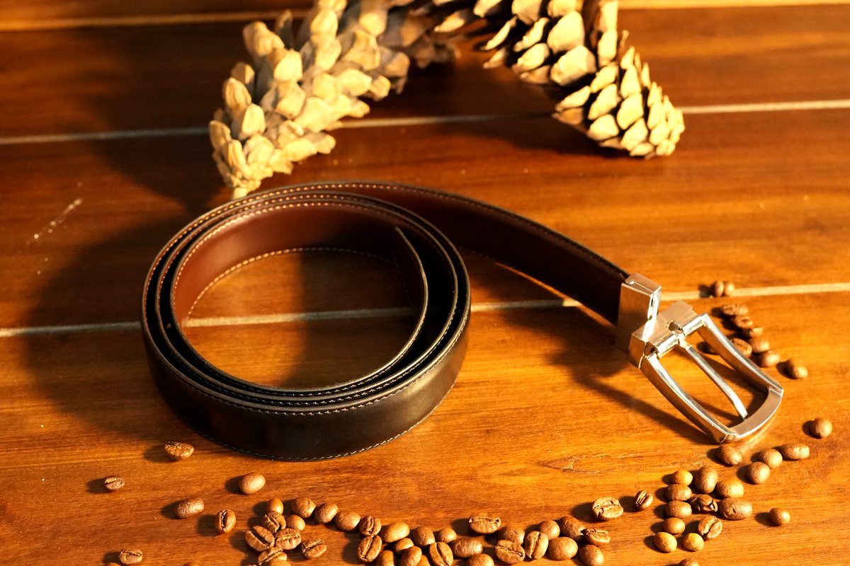 The Nova belt coiled beside a pine cone, coffee beans on walnut