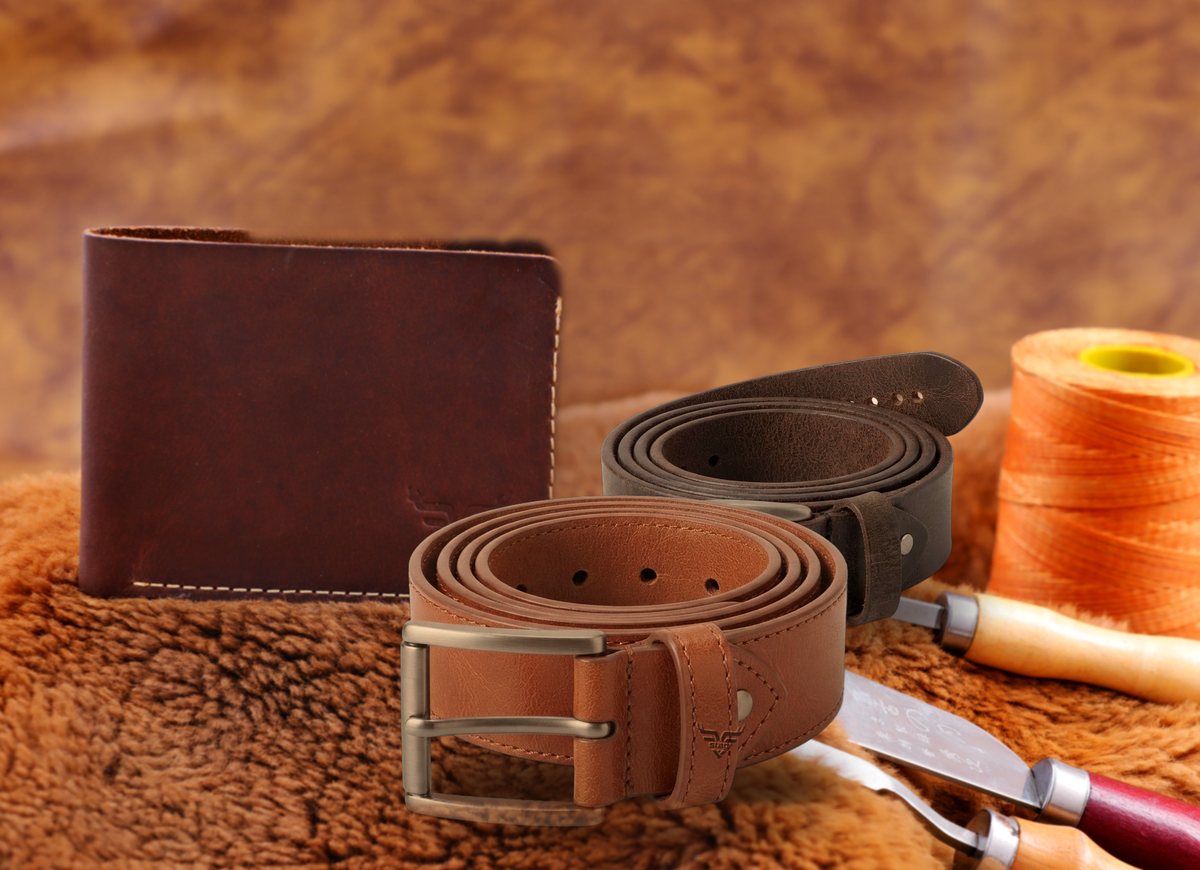 Two Stagr belts coiled in front of a bifold wallet, thread and tools on sheepskin